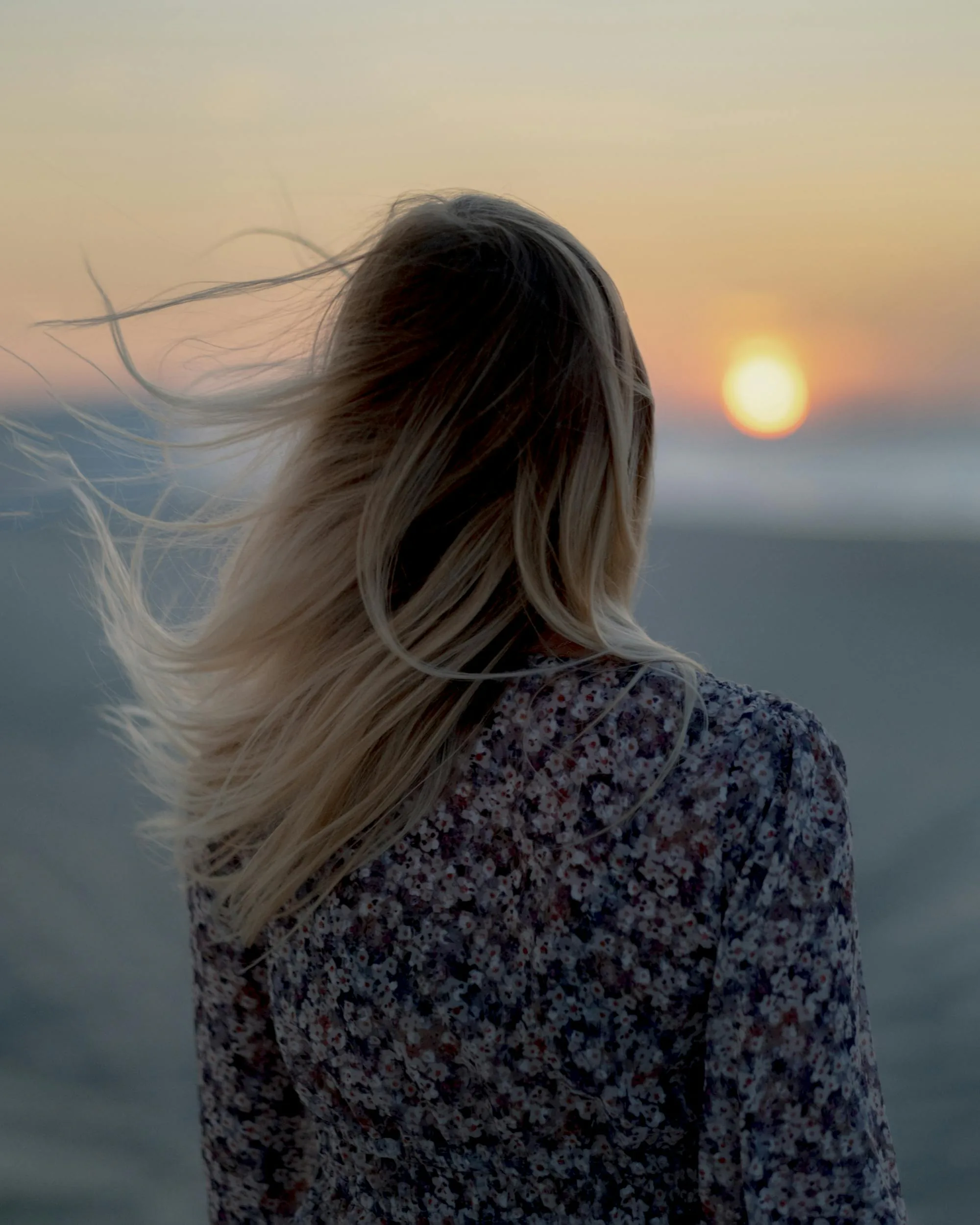 Cheveux au vent face à un coucher de soleil en bord de mer